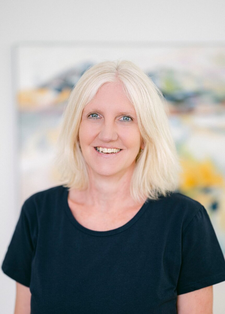 Frau Sinhart trägt weiß-blonde Haare und ein dunkelblaues T-Shirt. Sie blickt direkt in die Kamera.