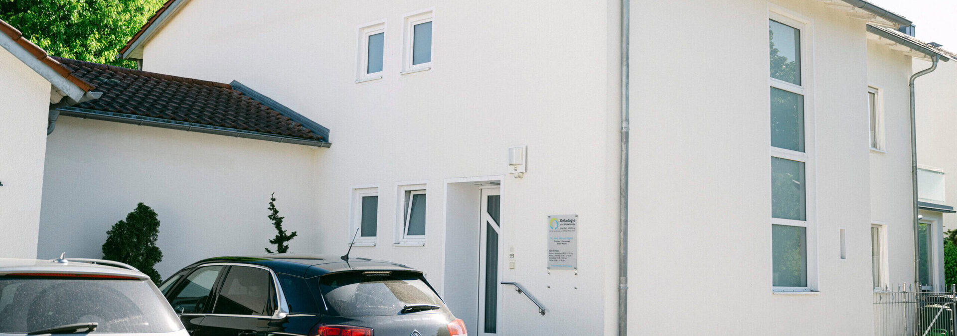 Außenansicht der Praxis. Ein weißes Haus mit vielen Fenstern ist zu sehen.