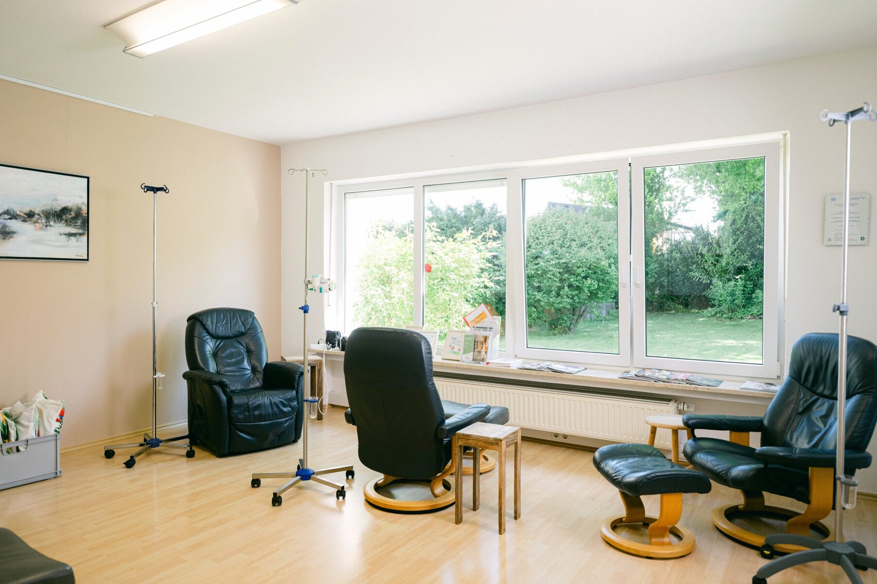 Ein Behandlungszimmer der Praxis ist zu sehen. Mehrere Sessel stehen aktuell leer und ein Blick aus den Fenstern zeigt einen schönen grünen Garten.