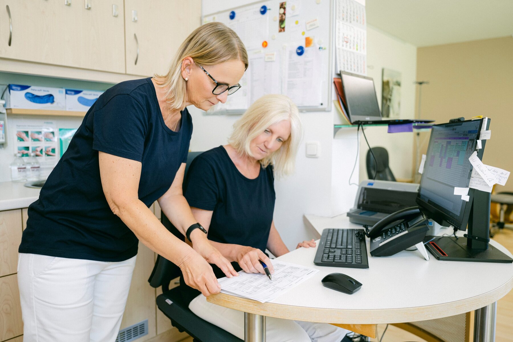 Zwei MFAs sitzen an einem Schreibtisch und prüfen einen ausgedruckten Bericht.