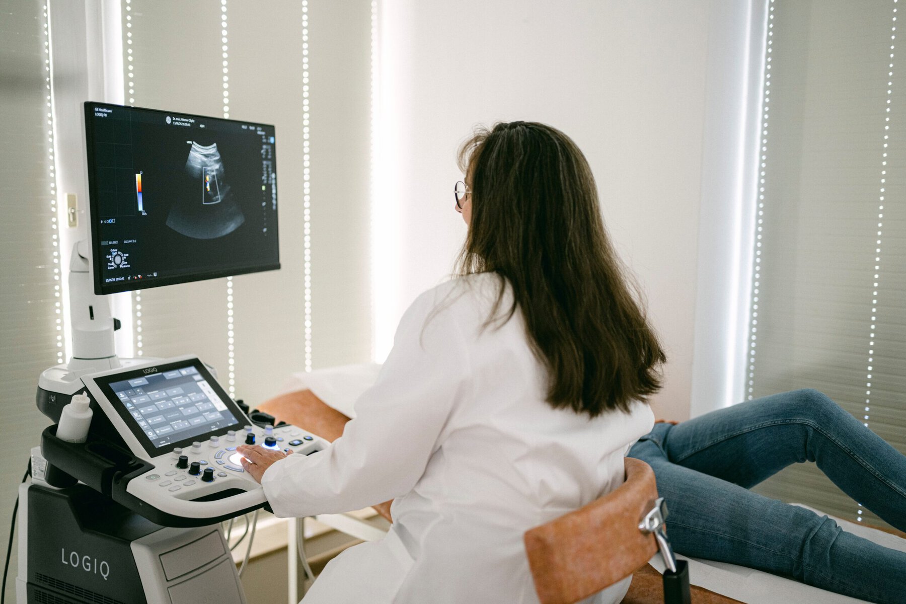 Frau Schäffer sitzt vor einem Ultraschallgerät und behandelt gerade eine Patientin, die auf einer Liege für die Untersuchung Platz genommen hat.